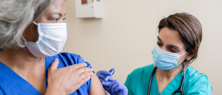 Photo of a health care professional giving a woman a vaccine with both wearing masks