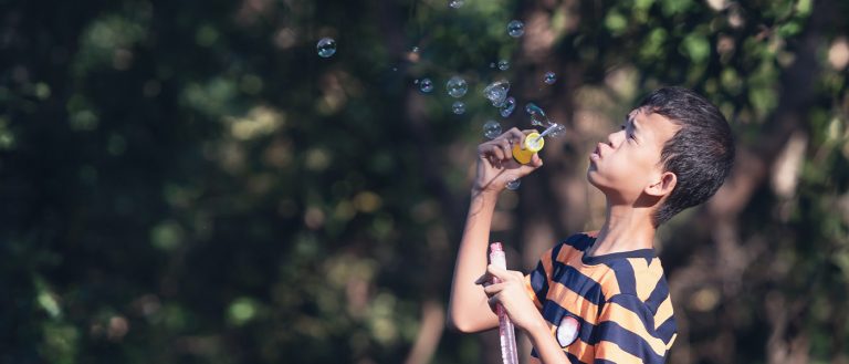 a young man blows bubbles at a paark