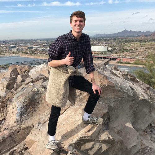 Photo of Bradley Schneider posing for a photo with a thumbs up on a mountaintop