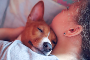 Photo of a teenager sleeping with her dog's head resting on her shoulder