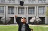 Photo of Spartie mascot wearing a graduation gown and tossing a cap in the air in front of Kelvin Smith Library