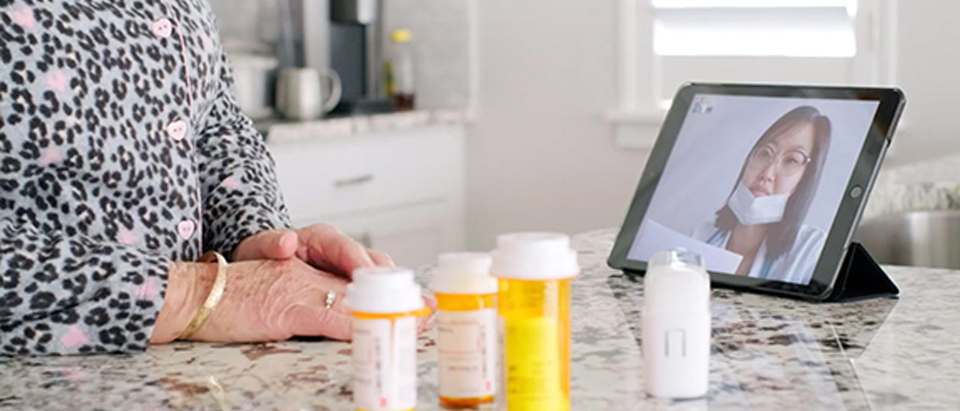 Photo of a patient in a video call with a nurse on a tablet with prescription bottles on the counter