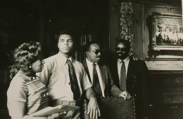 Black and white photo of Muhammad Ali visiting the Hanna Lounge as others stand nearby him
