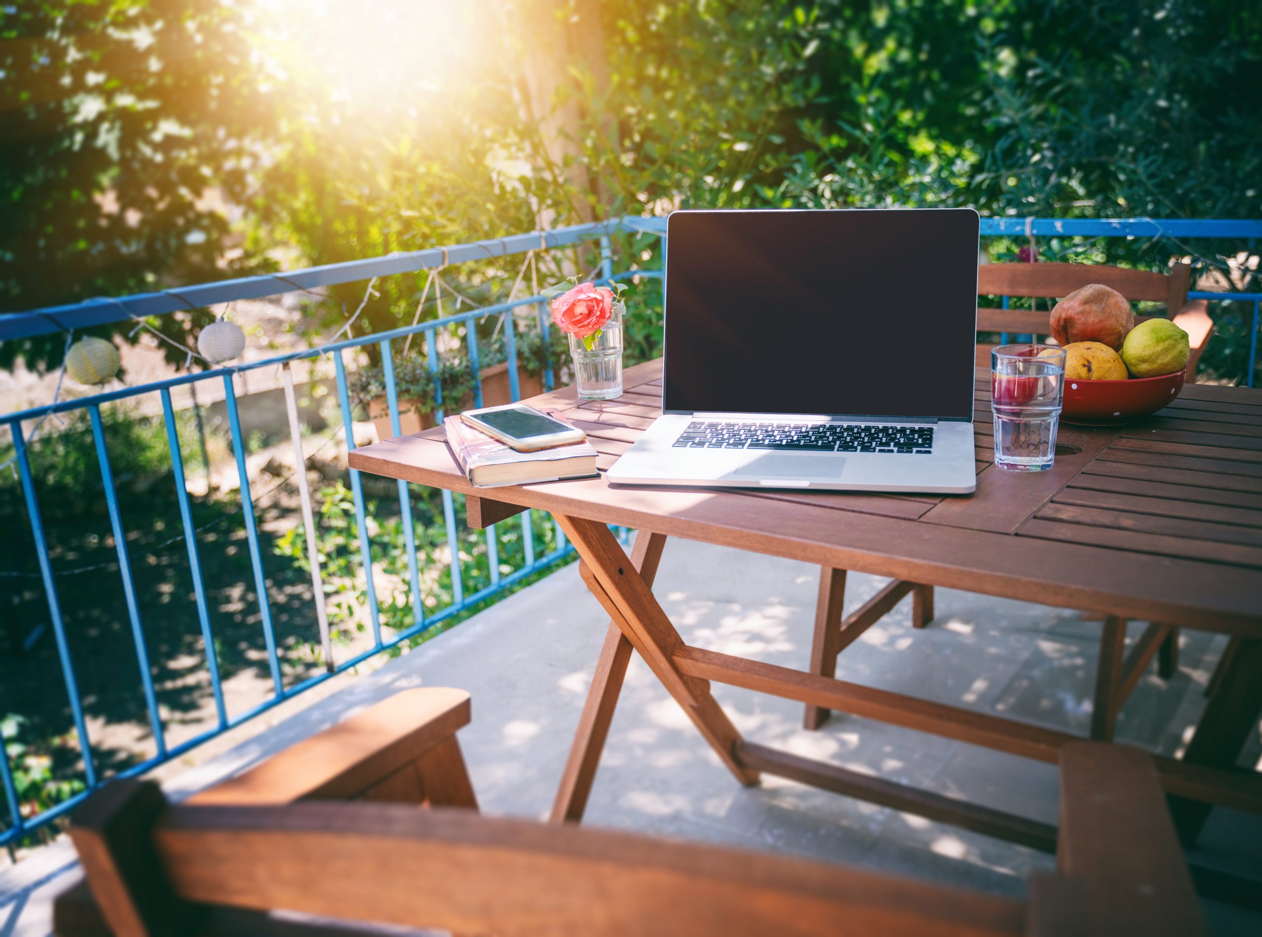Laptop on a wooden table on a sunny summer terrace, summer mood and vacation in a country house.
