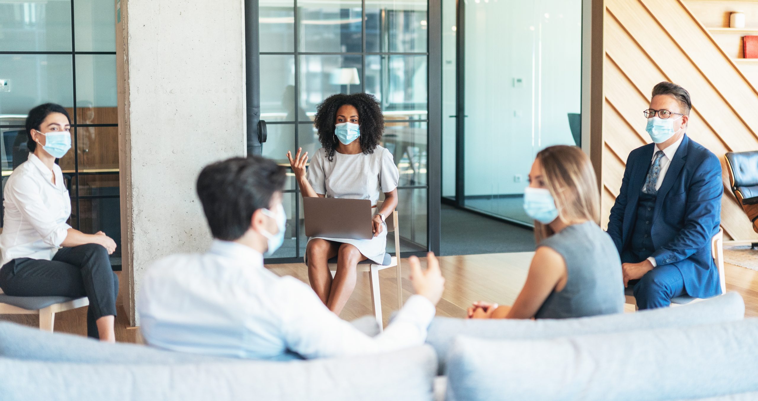 Business people on a meeting keeping distance and wearing face protective masks while discussing