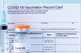 Covid-19 vaccine vial, vaccination record card, syringe, on a blue background.
