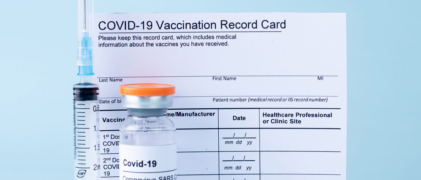 Covid-19 vaccine vial, vaccination record card, syringe, on a blue background.