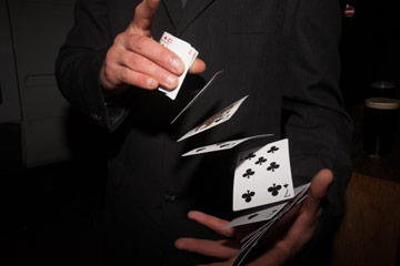 Photo of a magician shuffling cards midair from one hand to the other