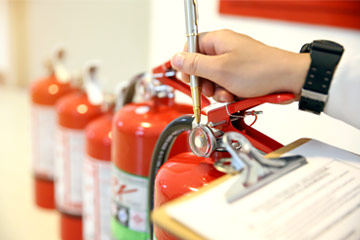 Photo of someone pointing to a fire extinguisher with a pen and holding a clipboard