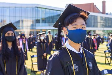 Photo of a CWRU graduate wearing a mask and looking ahead during commencement ceremonies with other graduates surrounding them