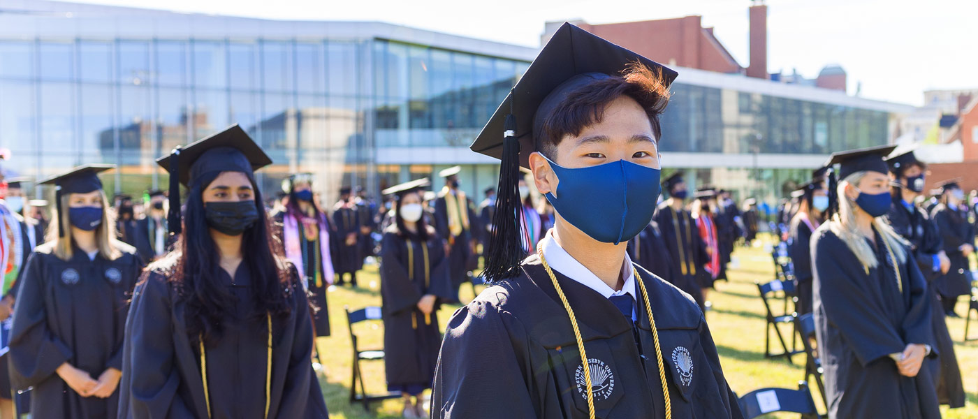 Photo of a CWRU graduate wearing a mask and looking ahead during commencement ceremonies with other graduates surrounding them