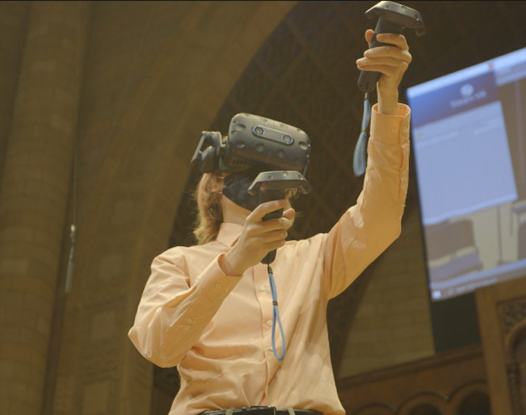 Photo of a student using a VR headset and controllers on the Maltz Performing Arts Center stage