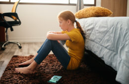 Little girl feeling depressed after reading text message on mobile telephone in home bedroom. Concept of bullying and loneliness among preteens