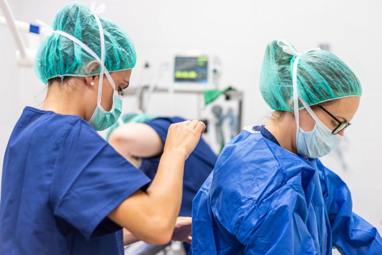 Medical assistant helping a surgeon put on sterile clothes in an operating room.