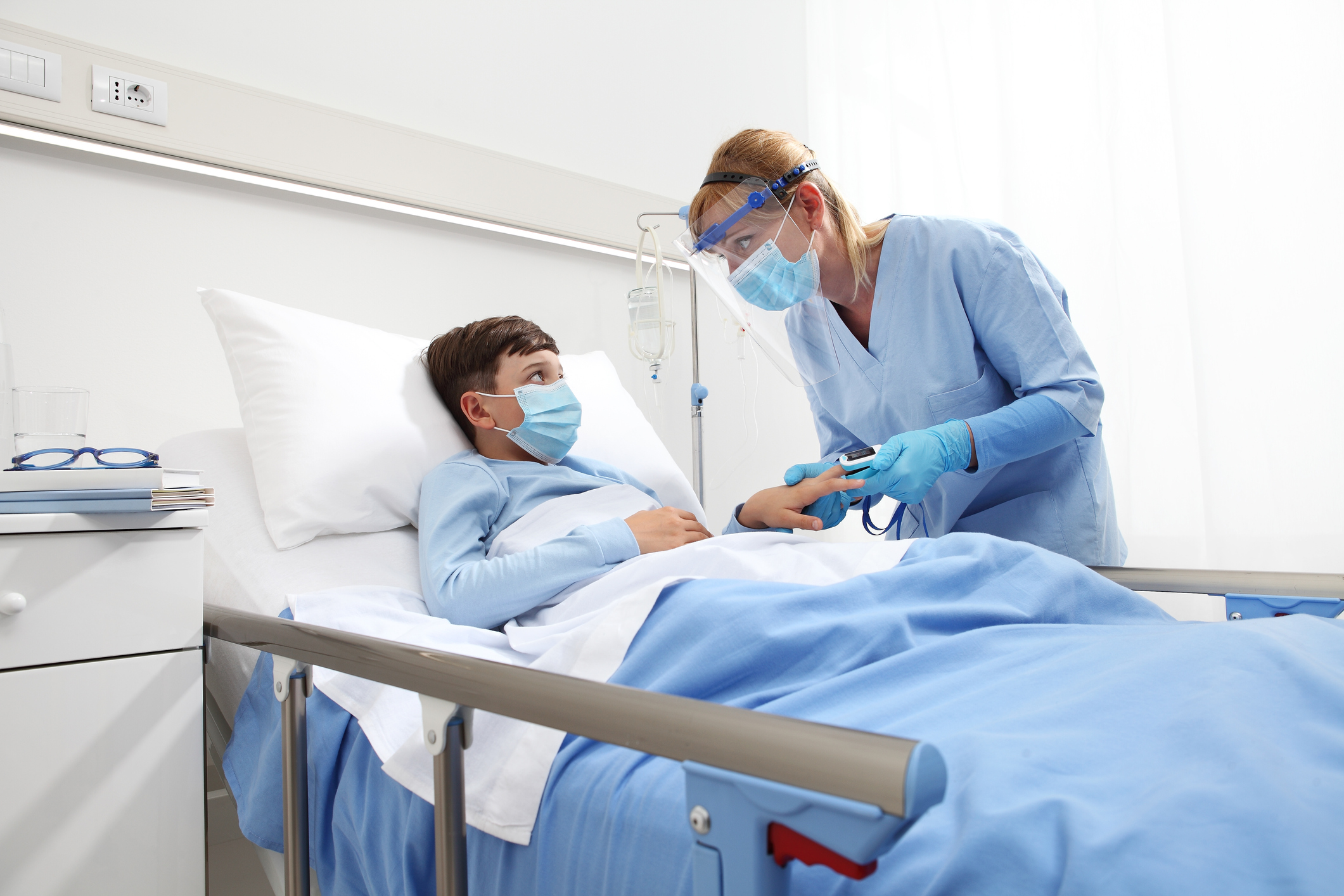 nurse with pulse oximeter on patient child in hospital bed, wearing protective visor mask, corona virus covid 19 protection concept,