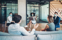 Group of entrepreneurs, wearing masks, sitting at a distance in the office and talking