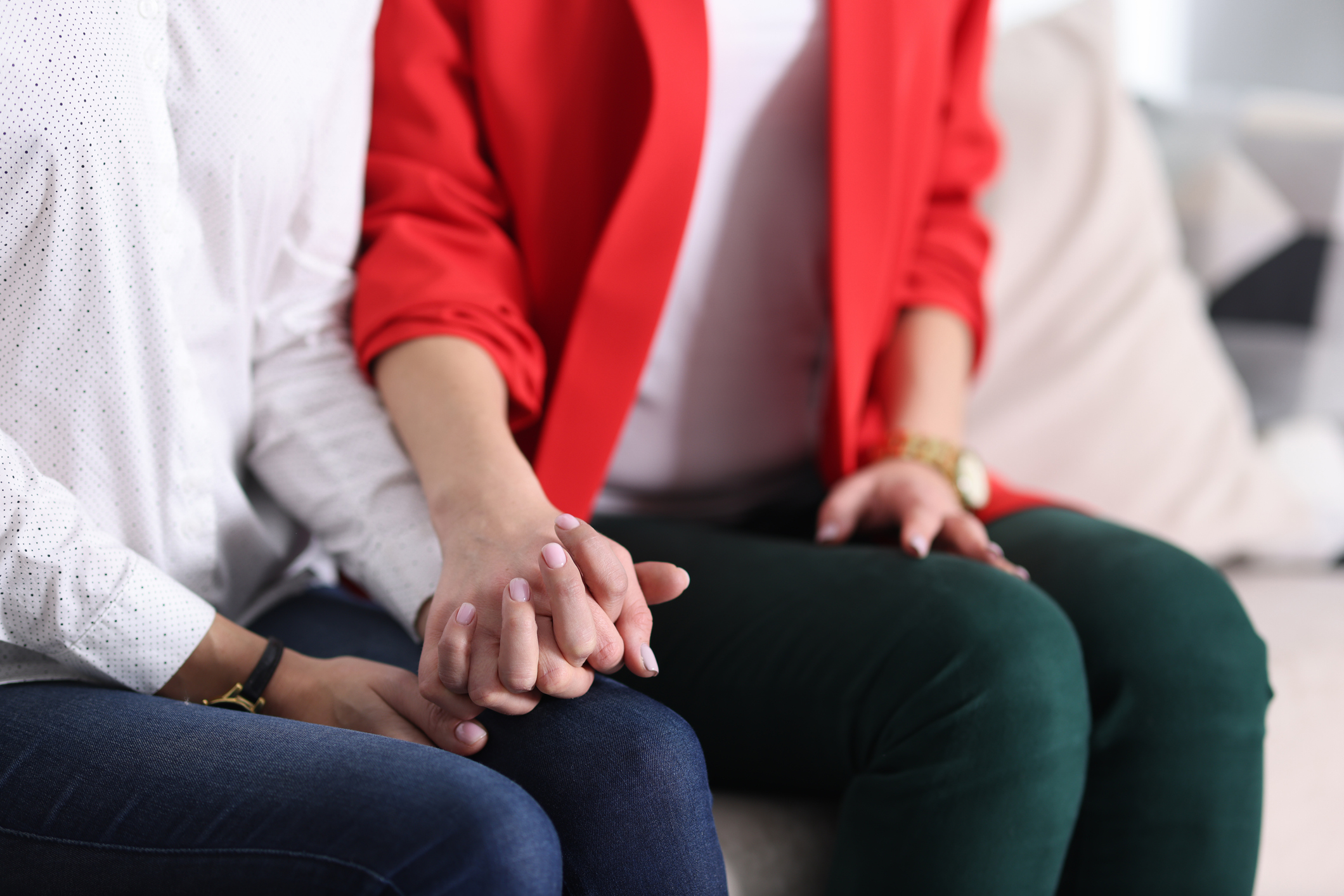 Two women tightly holding hands on couch at home close-up