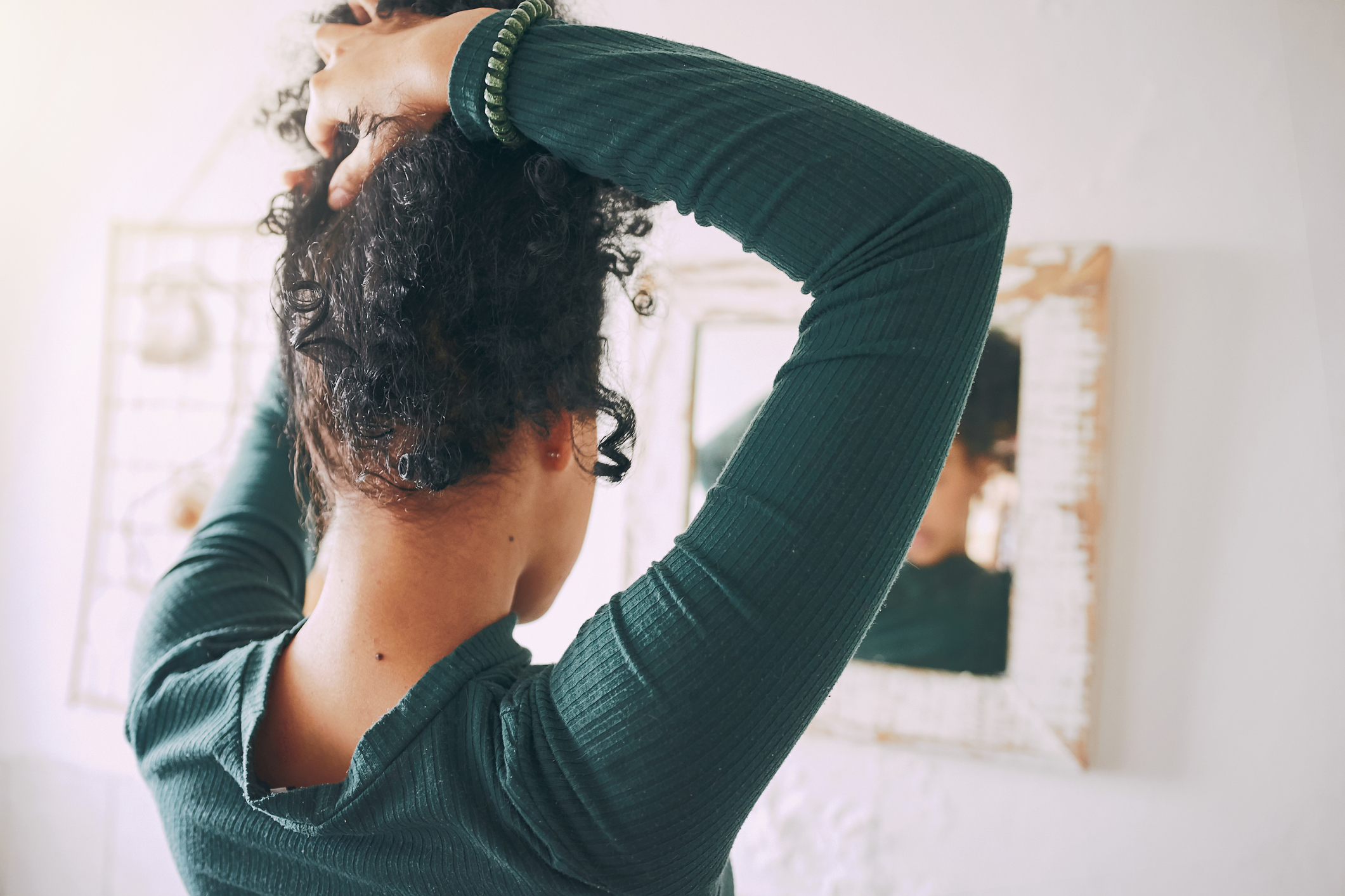 Rearview shot of a young Black woman tying her hair in the bathroom at home