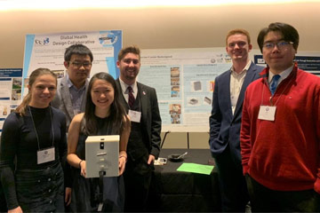 Photo of a group of students in Global Health Design Collaborative holding their vaccine carrier development in front of presentation posters
