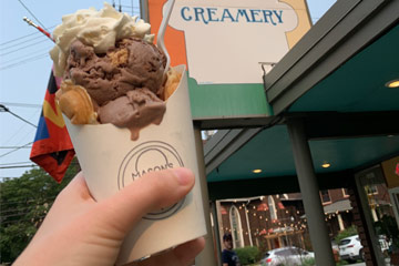 Photo of a hand holding up a cone of Mason's Creamery ice cream in an egg waffle next to the shop's sign
