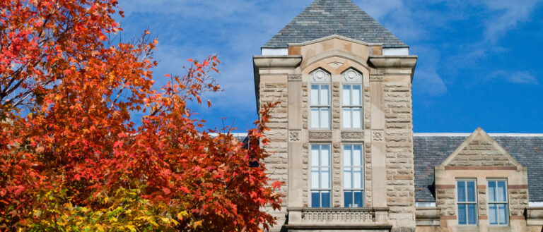 Photo of the top of Adelbert Hall with a tree with red leaves in the foreground