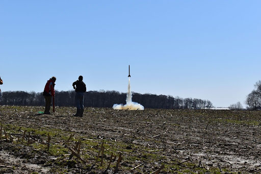 Photo of the Case Rocket Team launching a rocket in a field while two people look on