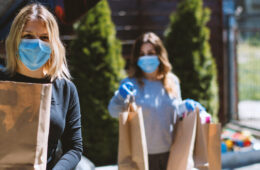 Photo of two women wearing masks and gloves holding paper bags of groceries