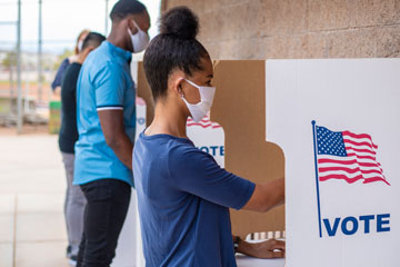 Photo of a young woman wearing a mask voting at a booth