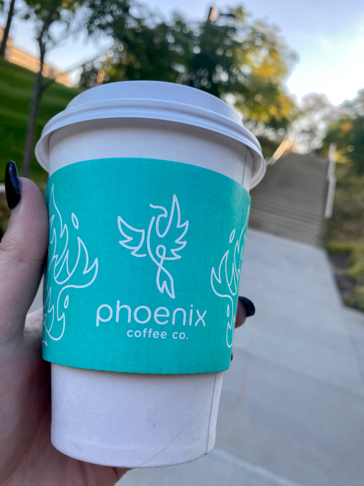 Photo of a hand holding up a to go cup of Phoenix Coffee
