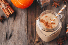 Photo of a pumpkin pie smoothie in a mason jar with a straw on a wood table