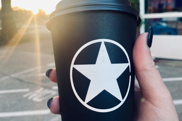 Photo of a hand holding up a Rising Star coffee to-go cup with sun beams shining down