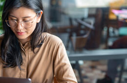 Asian Woman/ College Student Using a Laptop Computer to Study Remotely at a Cafe