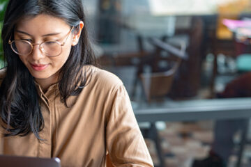 Asian Woman/ College Student Using a Laptop Computer to Study Remotely at a Cafe