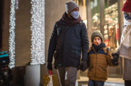 Photo of parents and a child holding hands as they leave a store dressed in winter clothes and masks