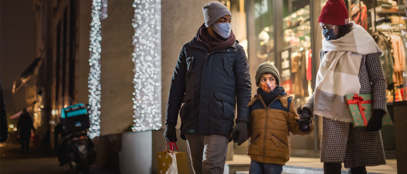 Photo of parents and a child holding hands as they leave a store dressed in winter clothes and masks