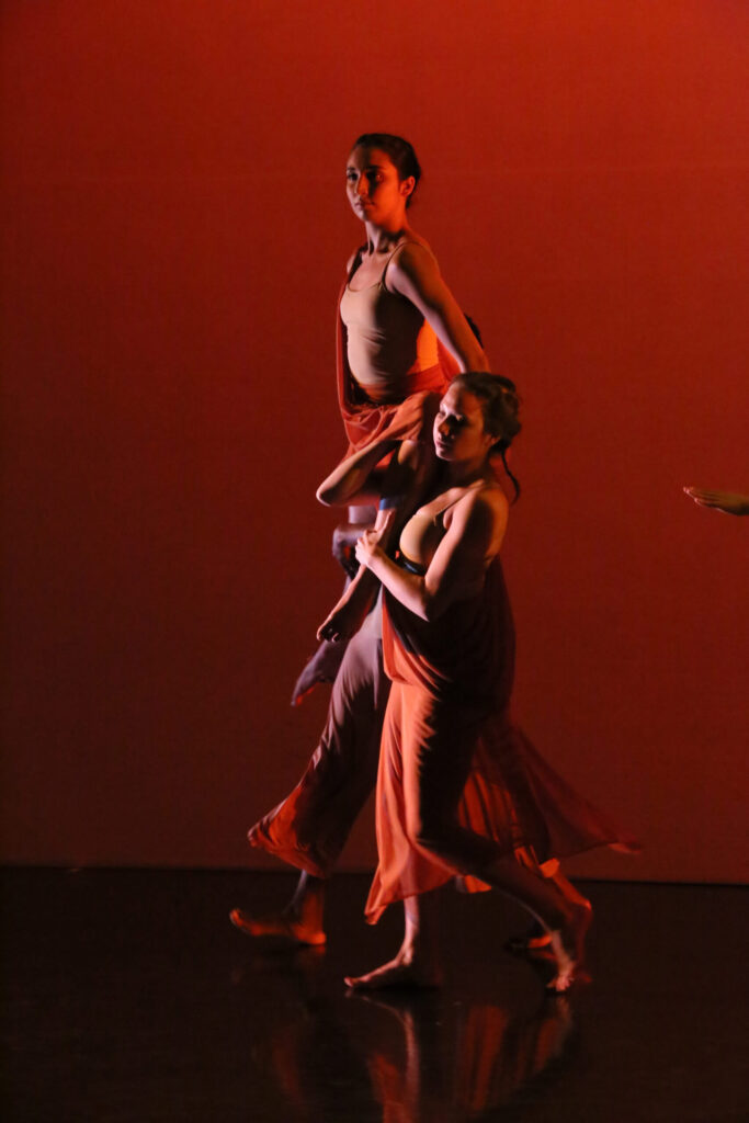 Photo of dancers holding up others in a red-tinged photo in MaDaCol dance
