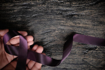 Photo of a hand holding a purple awareness ribbon