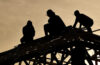 four workers atop a structure working at sunset