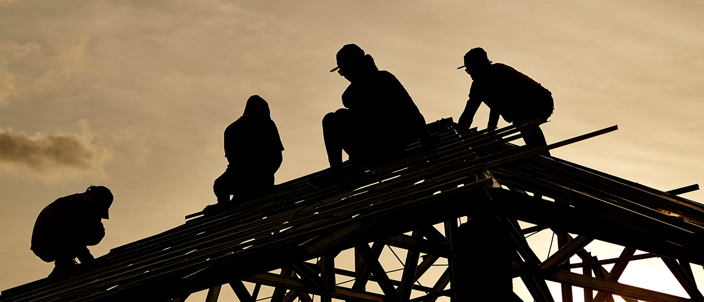 four workers atop a structure working at sunset