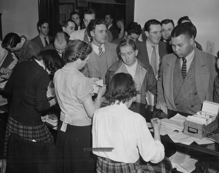 Black and white photo of students gathered around a table registering for classes at Adelbert College in the 1940s