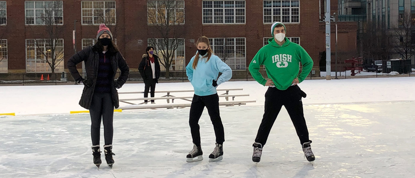 Photo of three students posing for a photo on the ice rink outside Veale Center