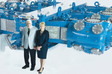 Photo of James P. Buchwald and Karen Buchwald Wright pose for a photo in front of a natural gas compressor