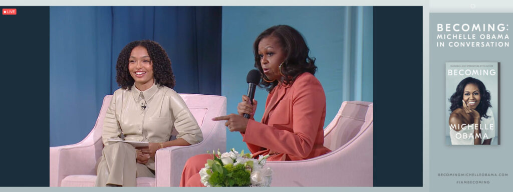 Photo of Michelle Obama speaking into a microphone seated next to Yara Shahidi at the Becoming event