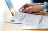 Photo of someone typing on a laptop with documents next to them