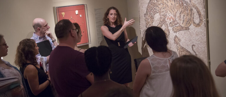 Photo of a faculty member leading a class as students gather around a piece at the Cleveland Museum of Art
