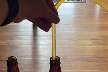closeup of a hand filling a beer bottle with a length of plastic tube