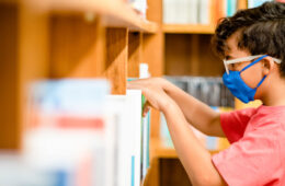 Photo of a child wearing a mask taking a book off a shelf