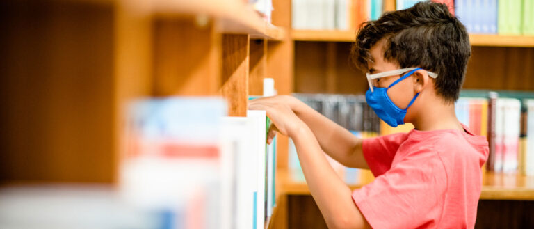 Photo of a child wearing a mask taking a book off a shelf