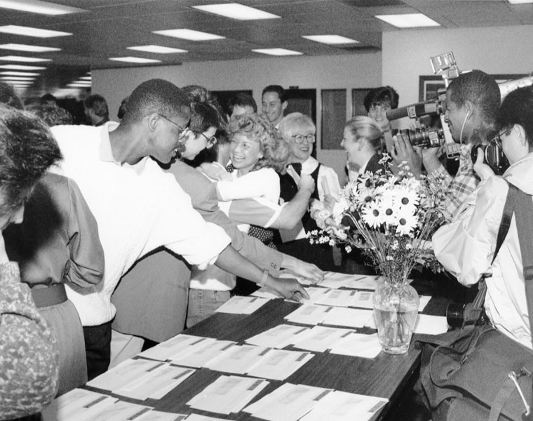 Black and white photo of a crowded room with the focus on a man grabbing a piece of paper off a table as part of Match Day at Case Western Reserve