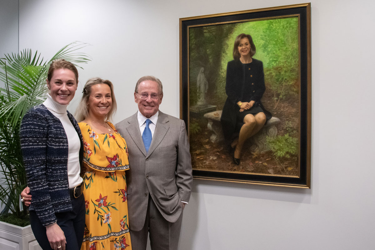 Kate Shaughnessy Biggar, Anne Shaughnessy Marchetto and Michael Shaughnessy stand next to a portrait of Marian Shaughnessy hanging on a wall
